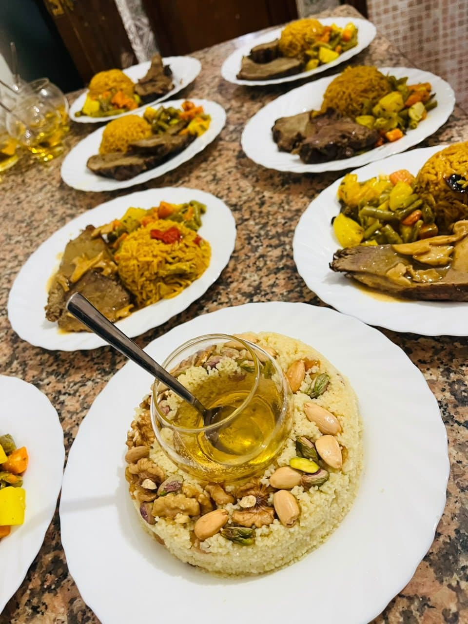 Des assiettes servies sur la table, avec au premier plan un couscous garni de fruits secs et de miel.