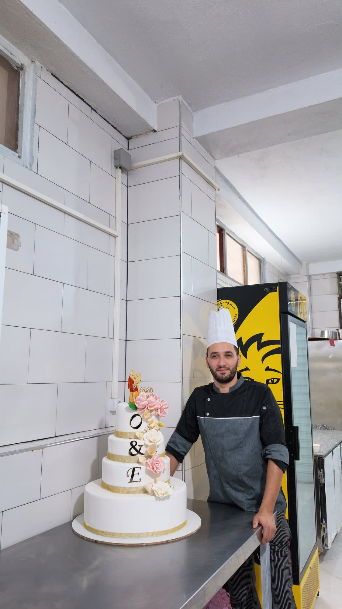 Un chef pose en cuisine à côté d'une pièce montée de mariage à quatre étages.