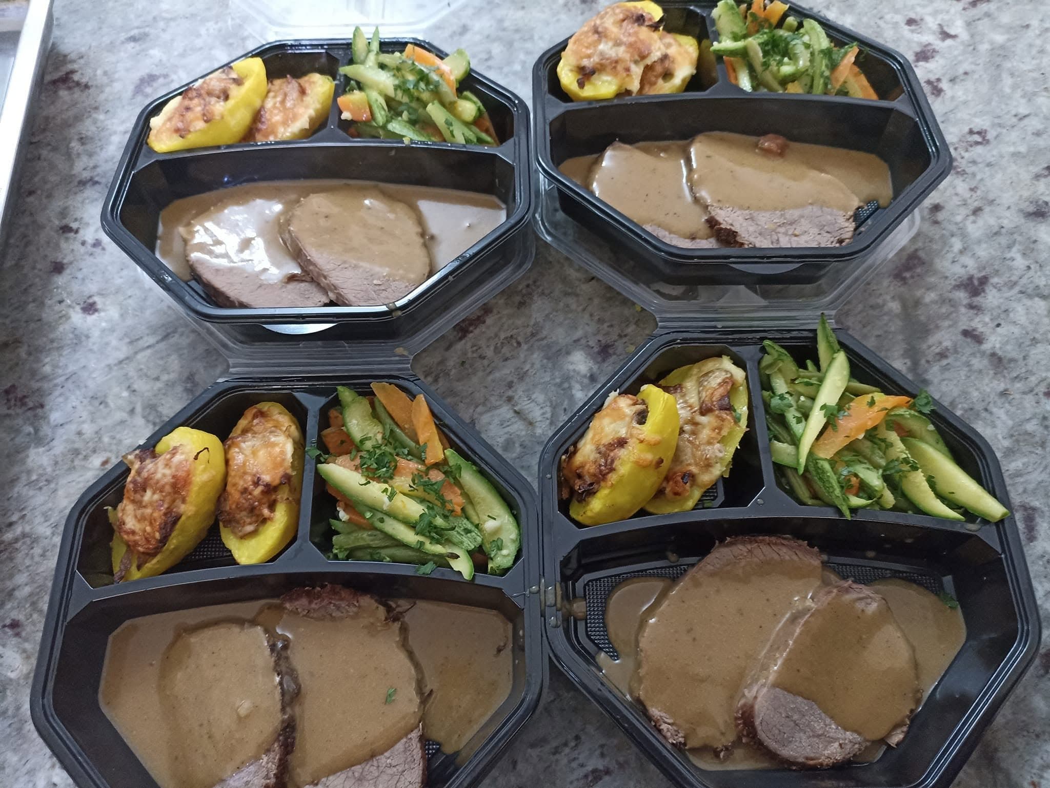 Quatre coffrets repas : viande en sauce, pommes de terre farcies et légumes sautés.