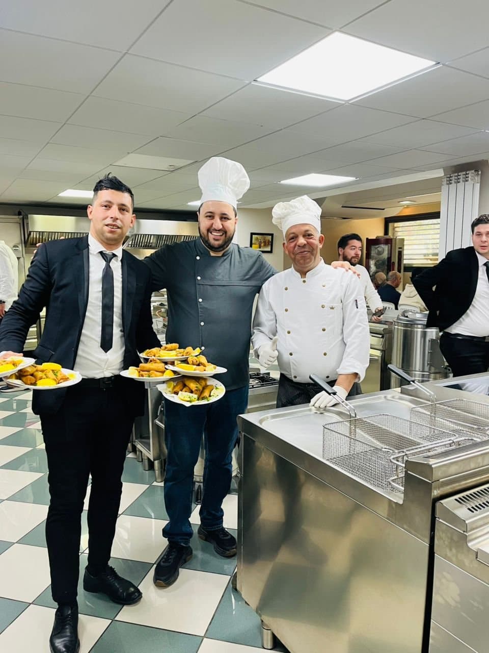 L'équipe en cuisine : deux chefs et un responsable de salle tiennent des assiettes prêtes à servir.