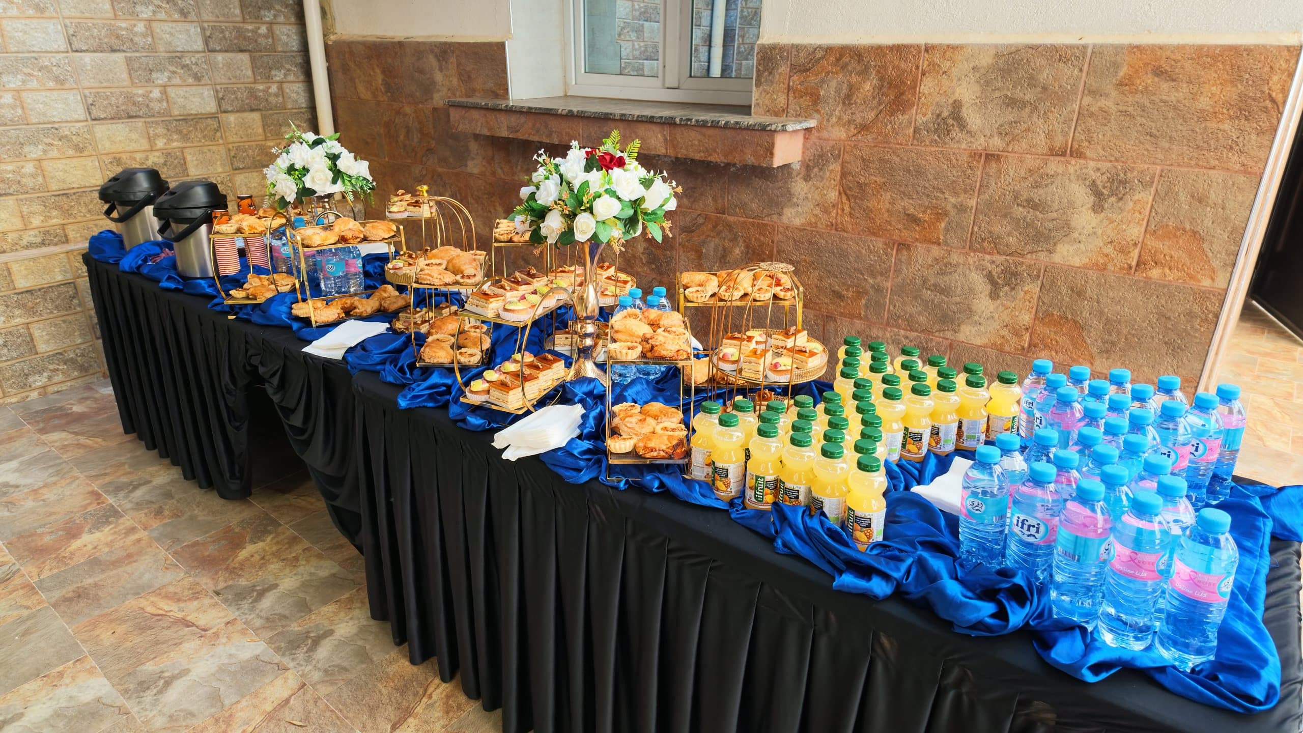 Une table de pause-café dressée : viennoiseries, jus, bouteilles d'eau et thermos de café.