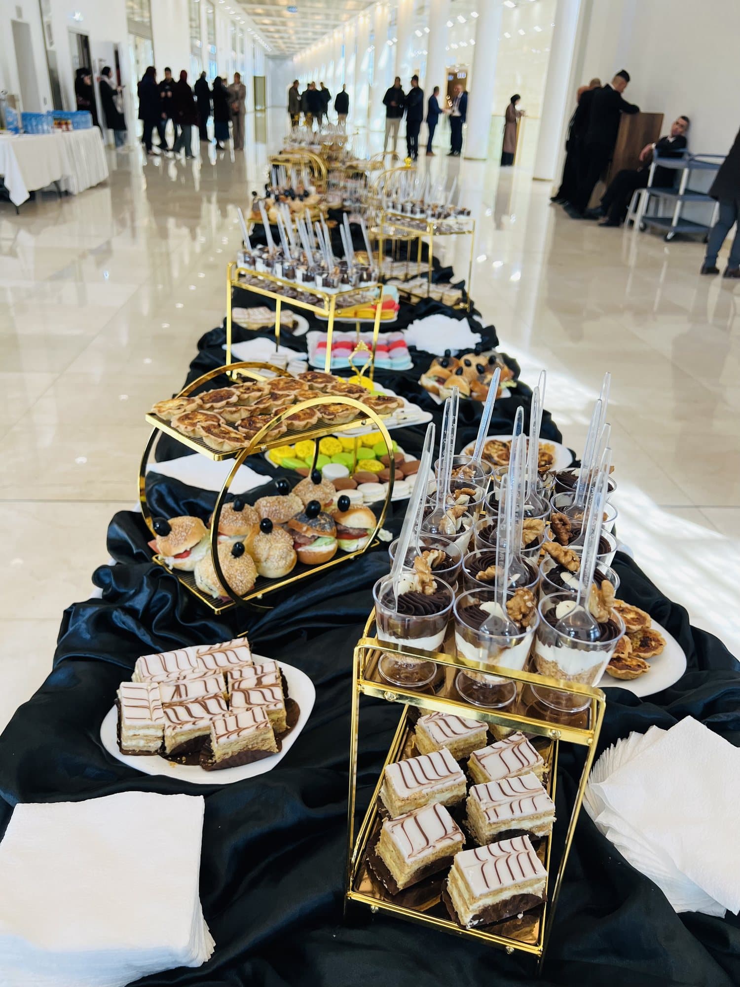 Un buffet de pause gourmande : verrines, mille-feuilles et petits gâteaux sur nappe noire.