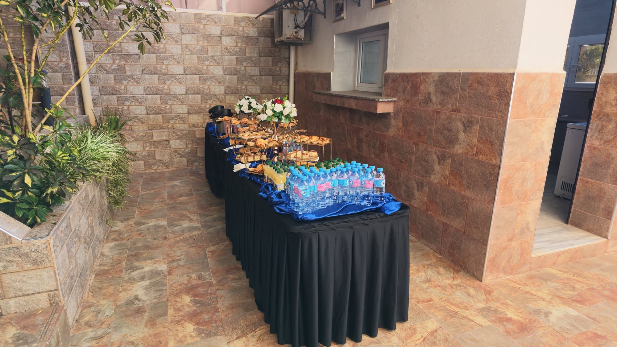 La même table après installation : viennoiseries sur présentoirs dorés, bouquets, jus et bouteilles d'eau.