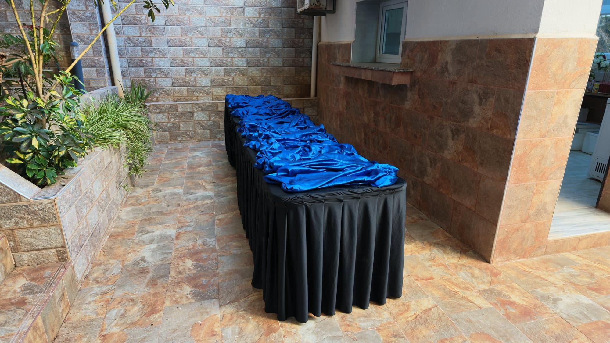 La table avant installation : nappe noire plissée et tissu bleu, encore vide, dans une cour.
